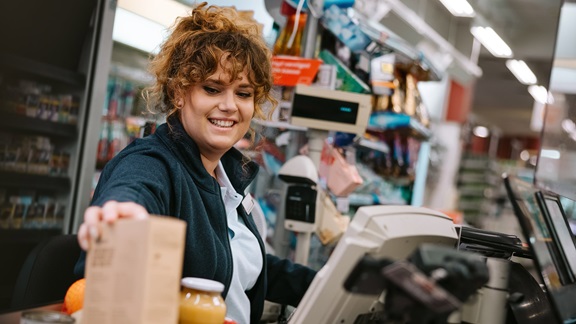 A curly-haired female cashier scanning customer's items at a grocery store