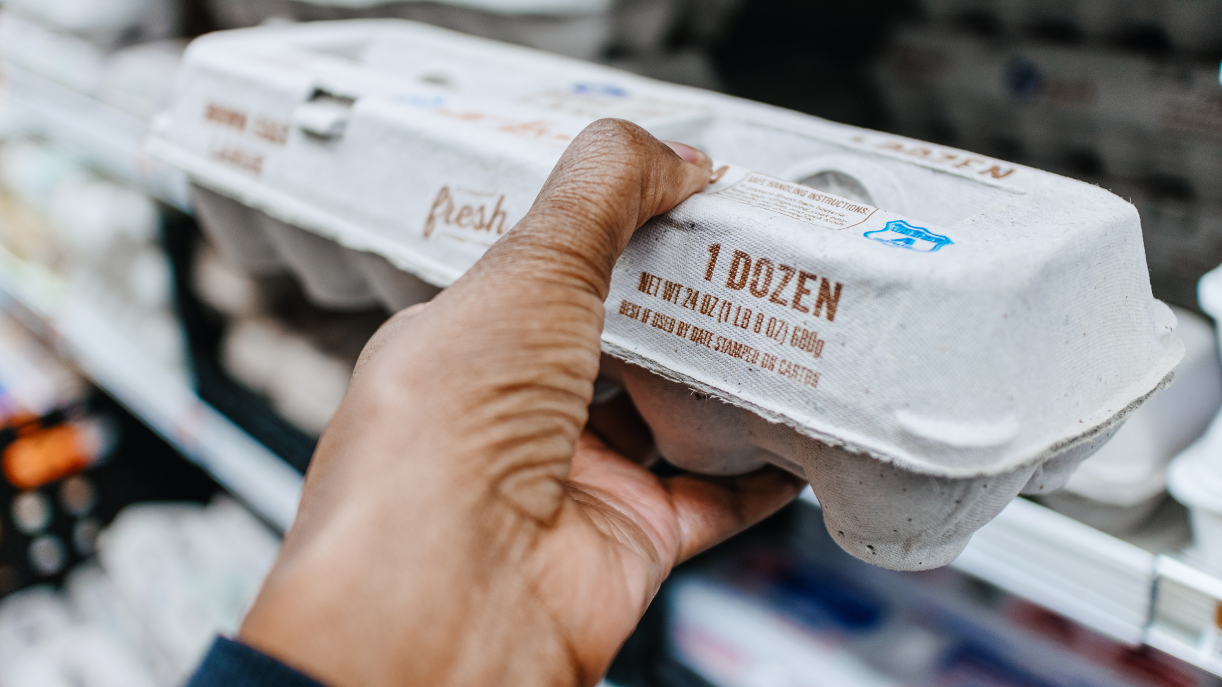 Close-up of a hand grabbing a carton of eggs from a refrigerated case in a grocery store