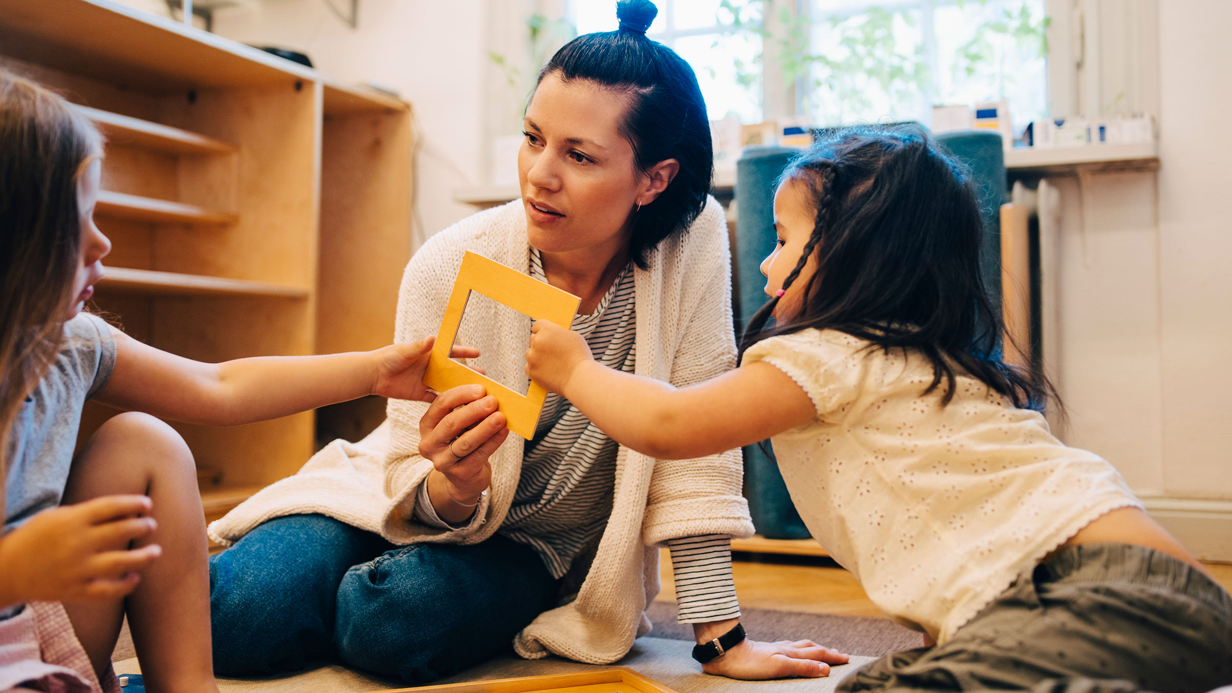 An in-home child care provider sits on the floor with two young children