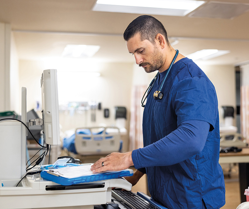 Male Nurse using a computer on a standing desk in a hospital setting