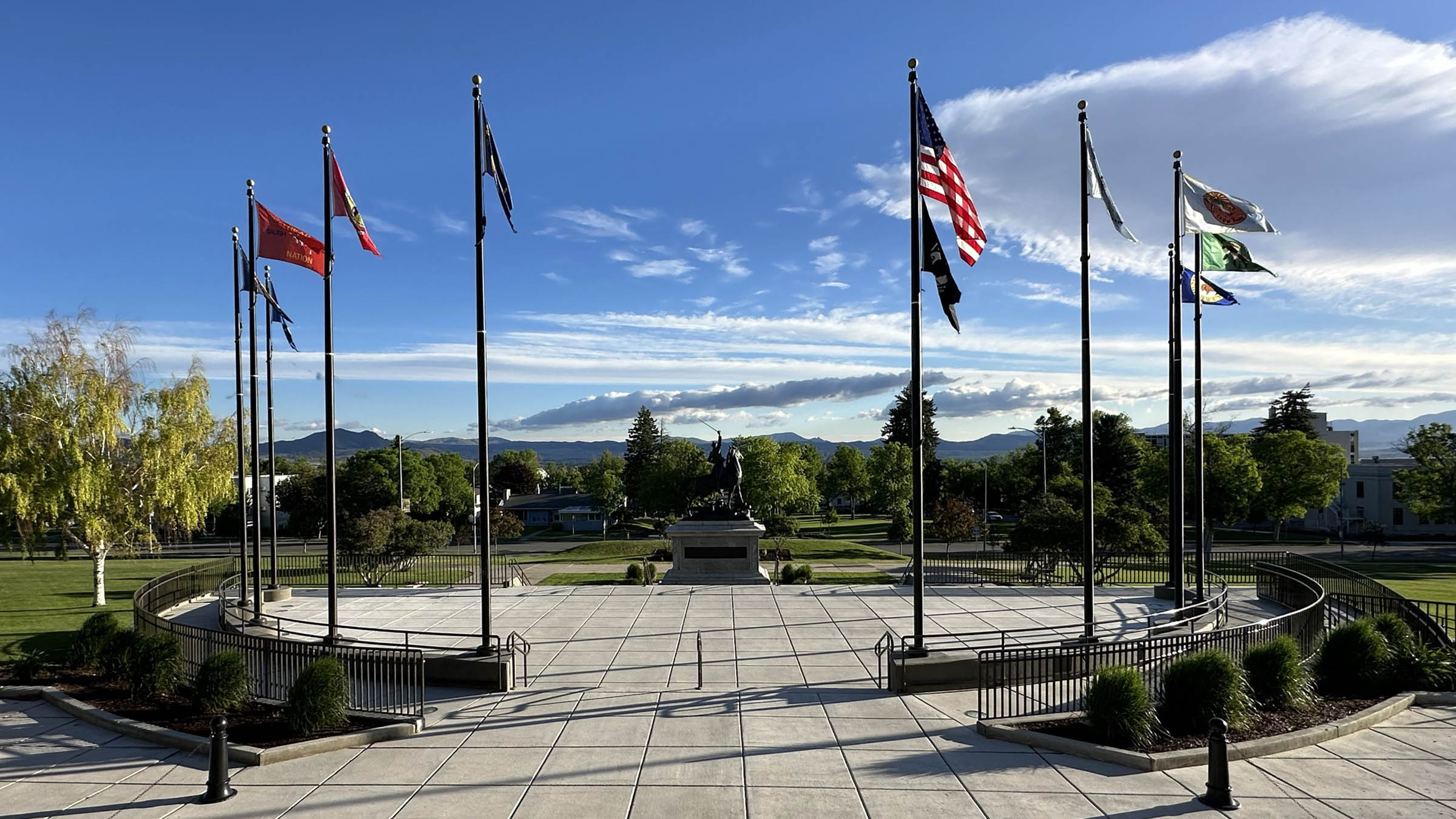 On a sunny day at the Montana State Capitol Tribal Flag Plaza in Helena, flags of the eight federally recognized tribal nations in Montana wave alongside the U.S. and State of Montana flags.