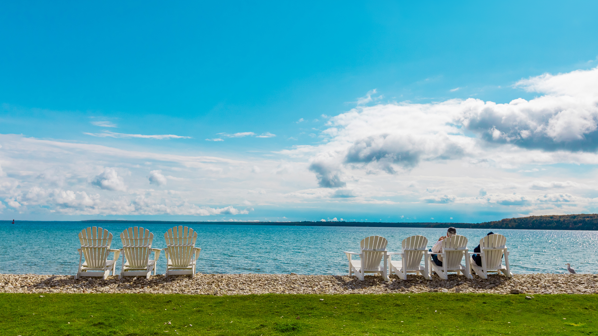 Groups of adirondak chairs facing a large lake, most of which are unoccupied