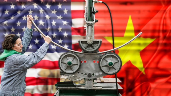 Manufacturing worker bending metal rod with machinery, with American and Chinese flags in the background