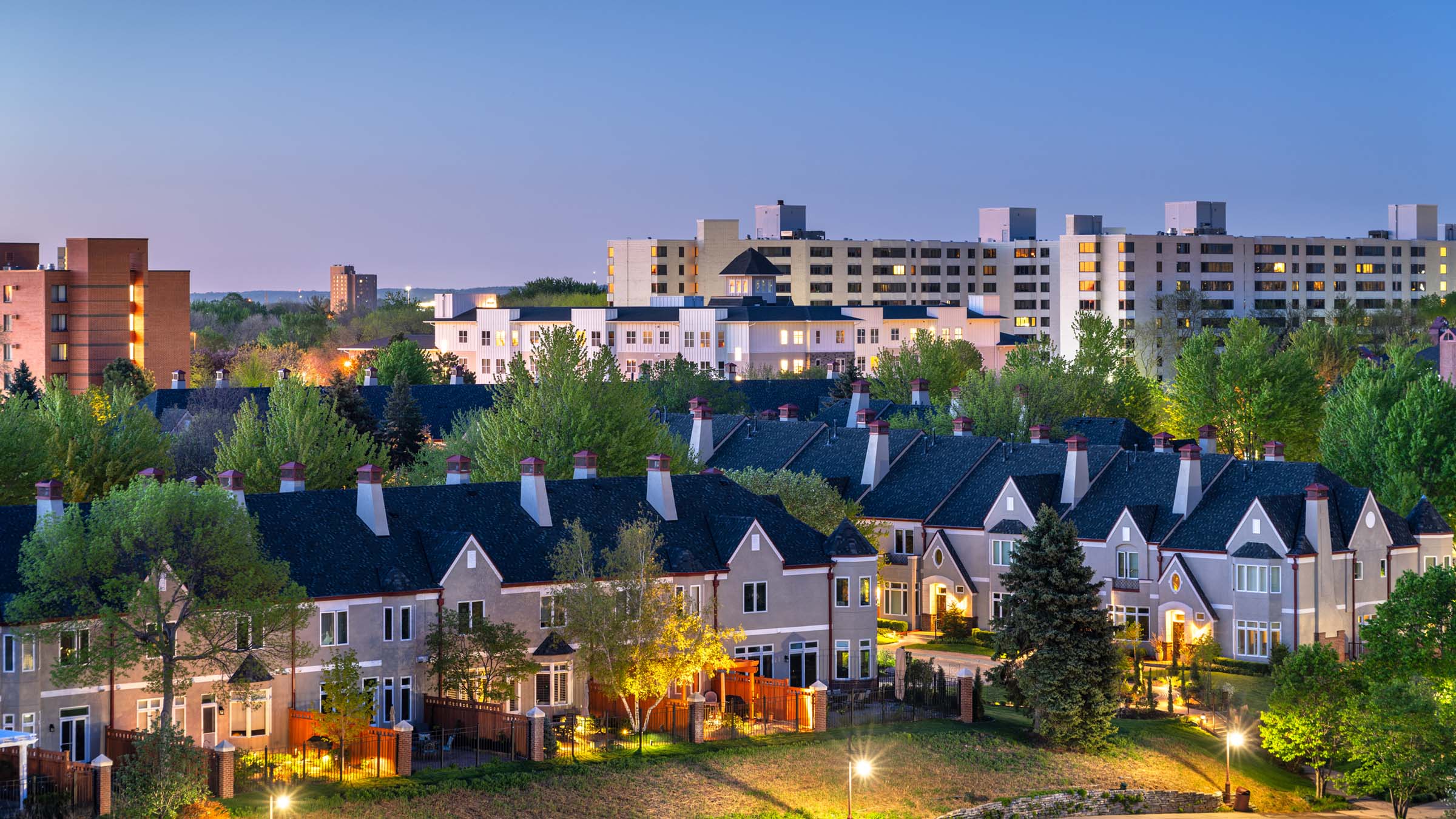 Part of the Minneapolis suburb of Edina, Minnesota, is seen in the early morning light on a clear spring day. The foreground shows a townhome development, the middle ground shows a newer-construction apartment building for seniors, and the background shows a midrise condominium building.